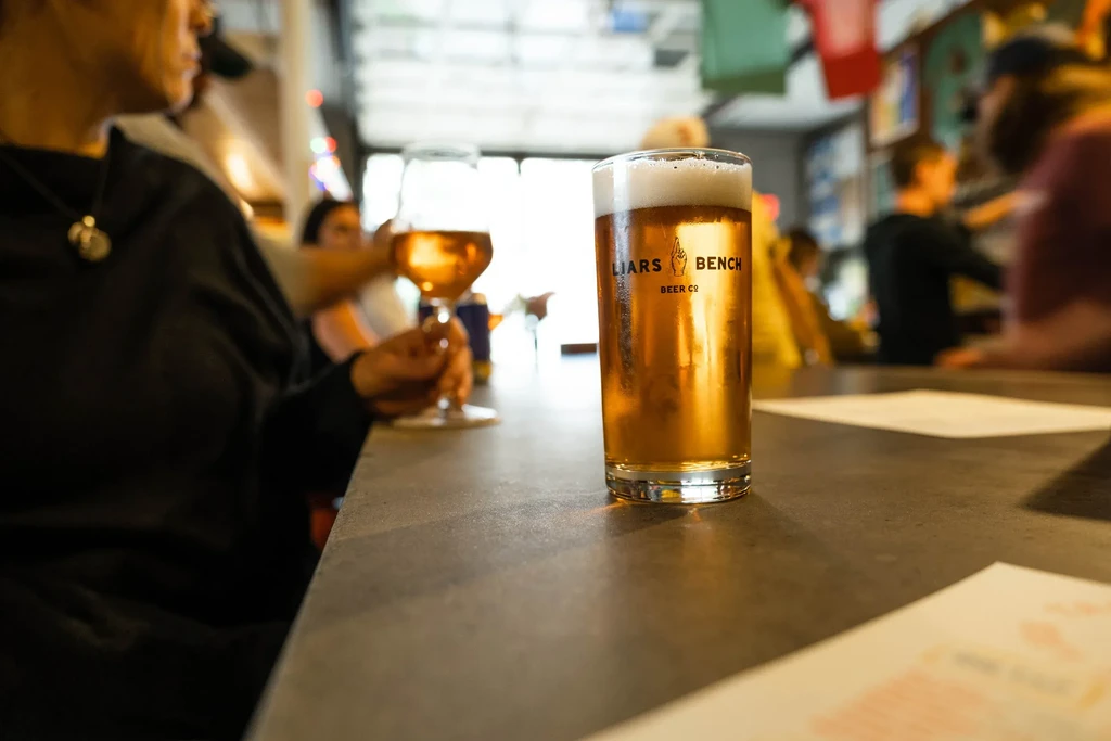 Close-up of Liars Bench beer glass with foam on a dark bar table.