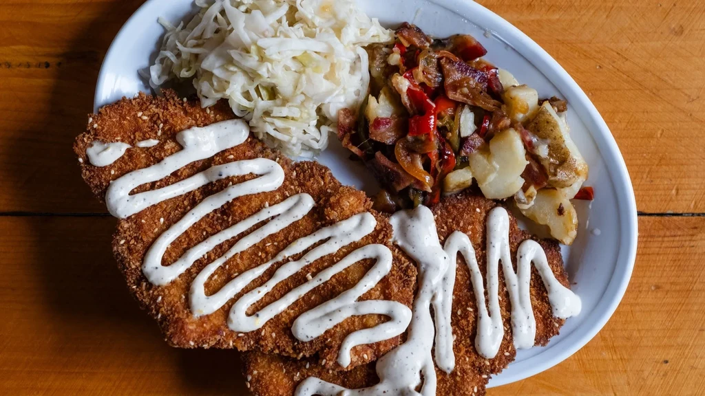 Oval plate with breaded cutlets, creamy sauce, shredded and roasted vegetables.
