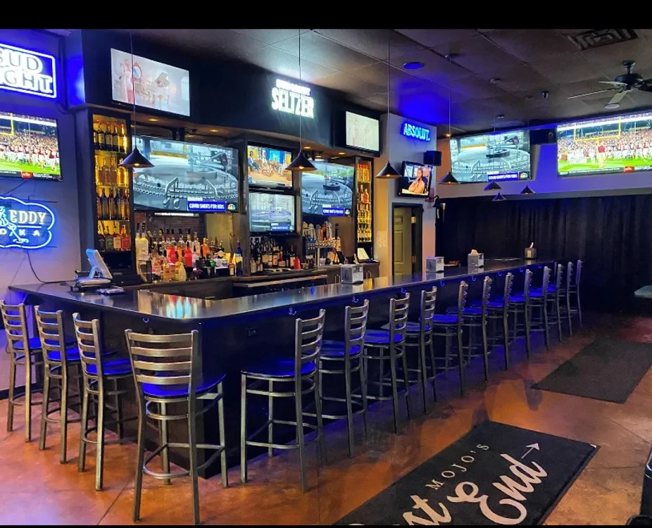 Empty modern sports bar, illuminated bottles, neon signs, and TVs.
