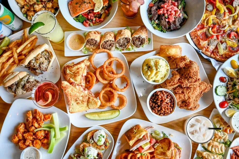 Overhead view of a diverse feast of fried chicken, pizza, and drinks.