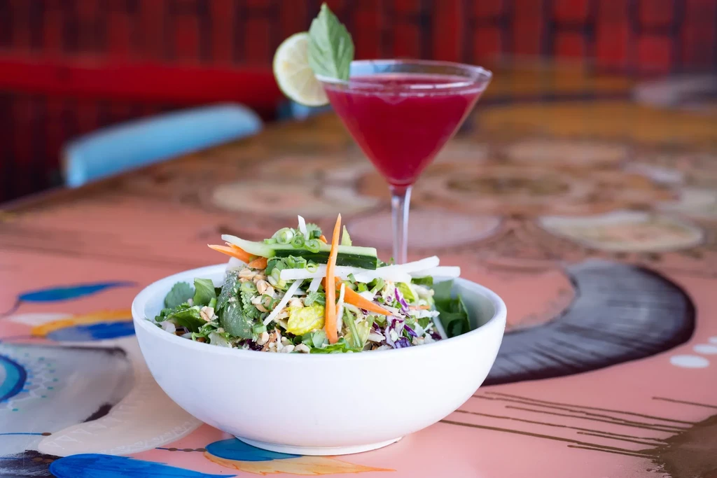 Vibrant salad with nuts and red cocktail on a colorful restaurant table.