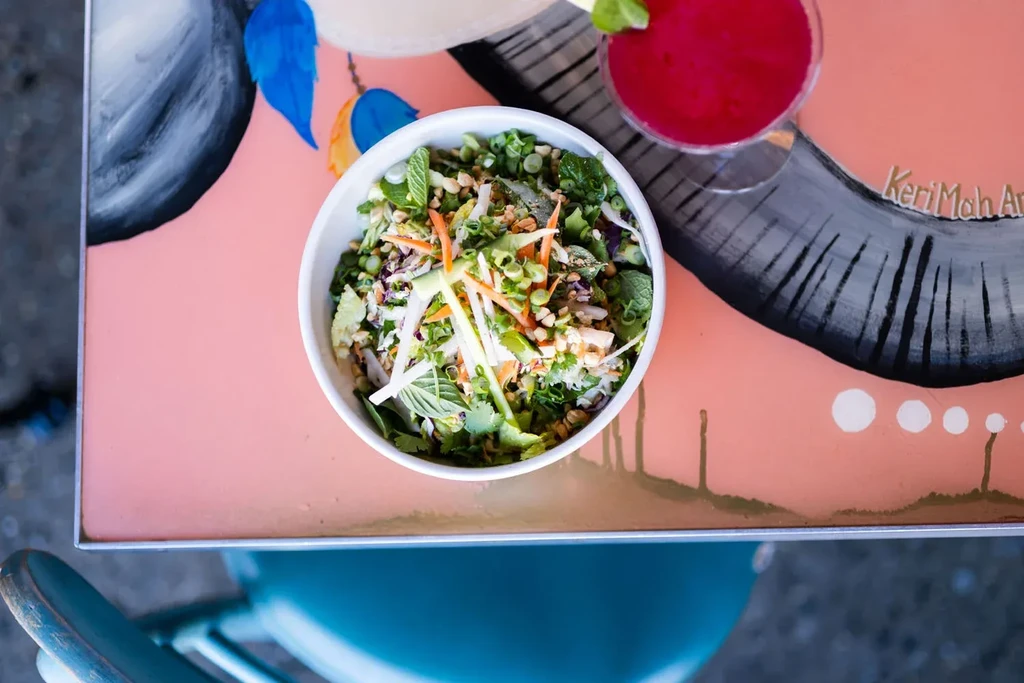 Overhead: vibrant salad, red cocktail, on an abstract KeriMah Art table.