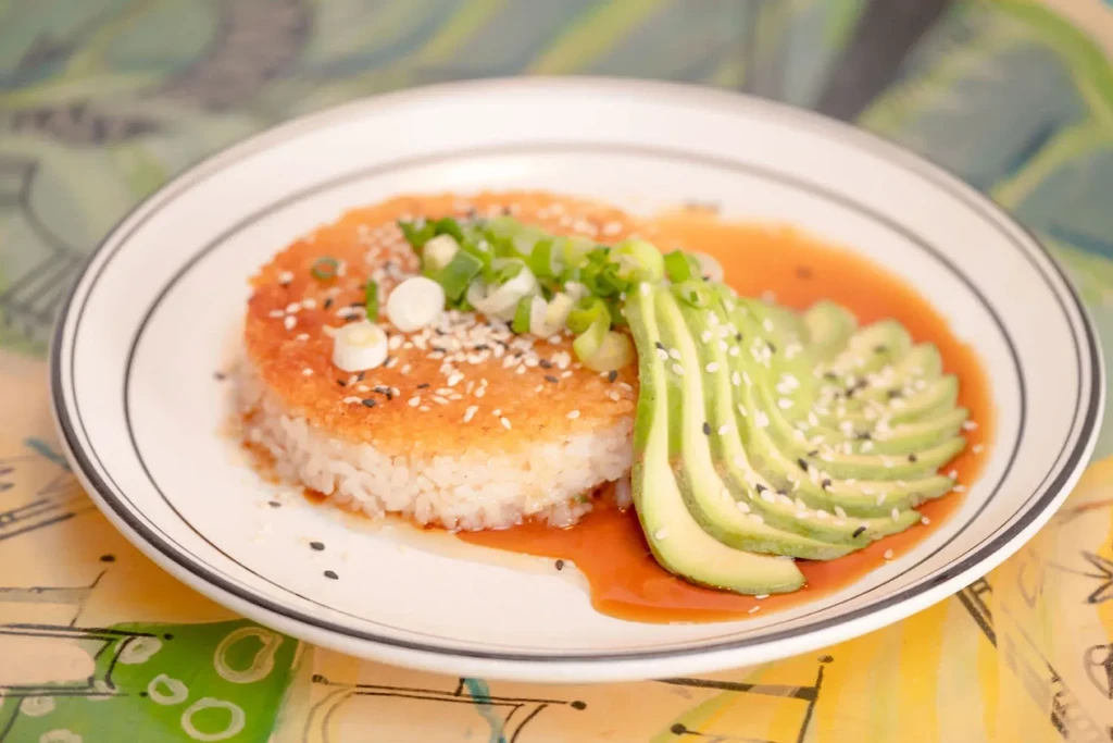 Golden-brown seared rice patty, fanned avocado, sesame seeds, and sauce.