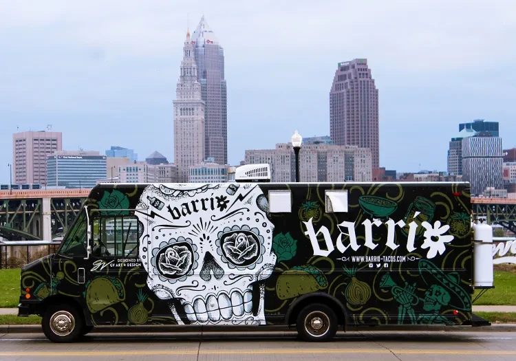 Food truck with sugar skull, 'Barrio' text, parked on urban street.