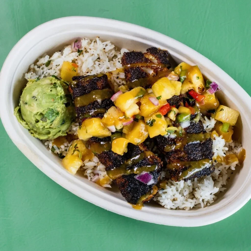 Disposable bowl with seared protein, rice, pineapple salsa, and guacamole.