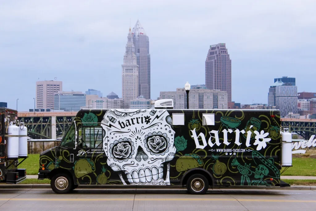 Vibrantly decorated Barrio food truck with sugar skull, in Cleveland cityscape.
