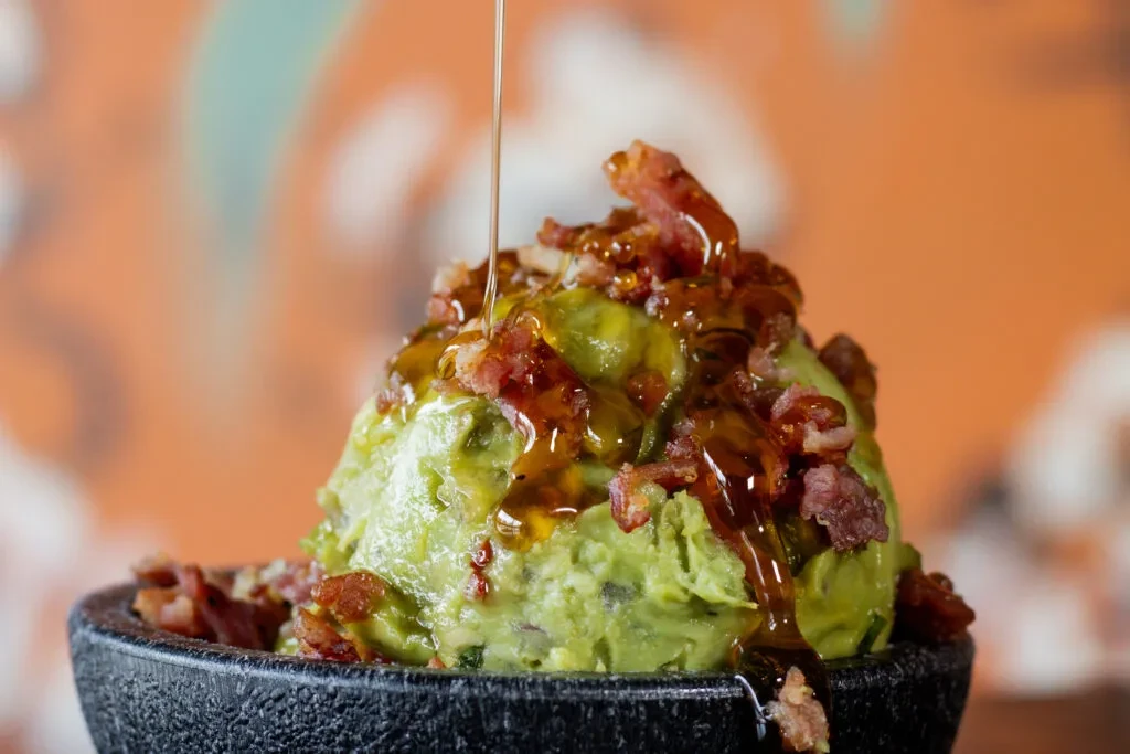 Guacamole in molcajete with bacon and pouring golden honey.
