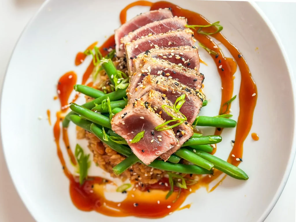 Seared tuna with sesame crust, green beans, rice, and sauce.