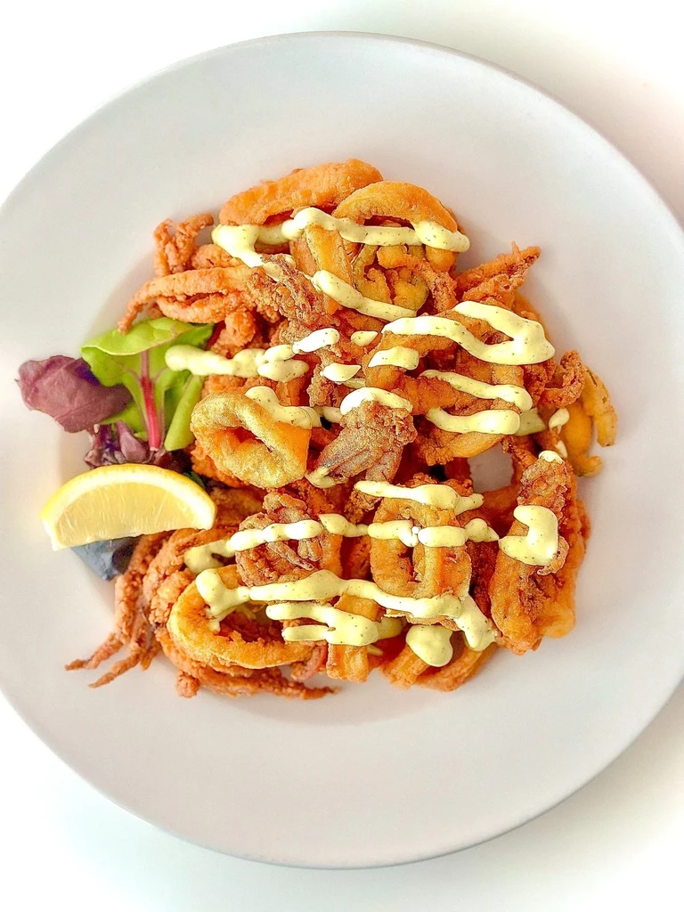 Crispy fried calamari with creamy sauce, lemon, and salad garnish.