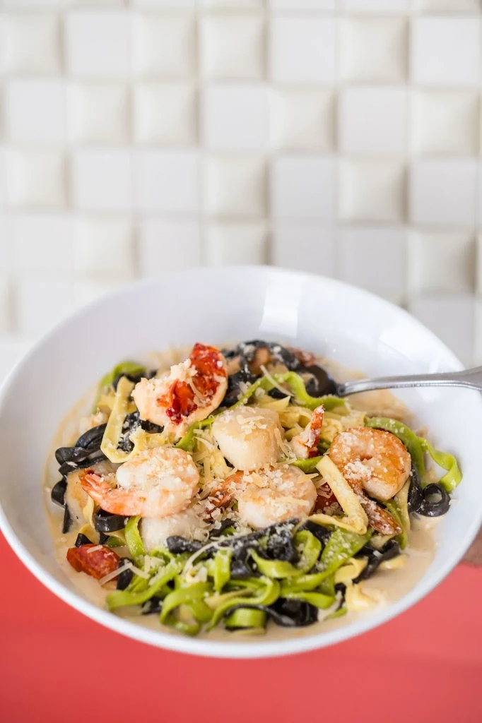 Close-up of colorful seafood pasta with dark and green noodles, shrimp, and cheese.