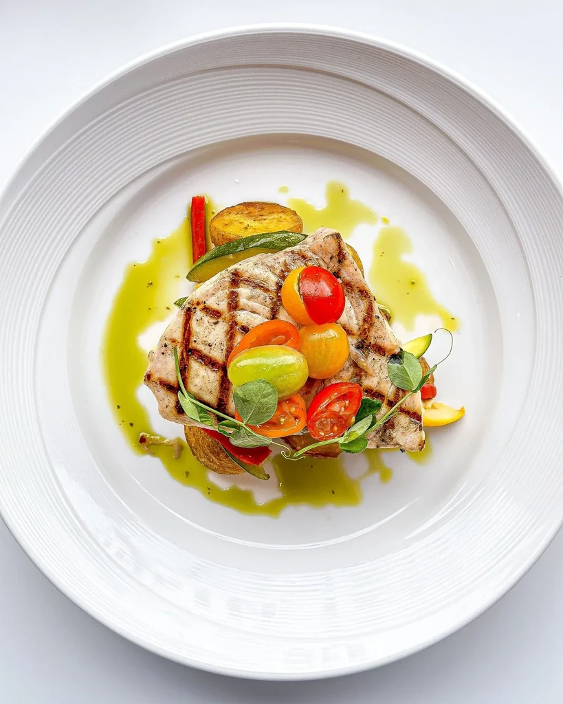 Grilled fish or chicken, roasted potatoes, colorful tomatoes, and green sauce.