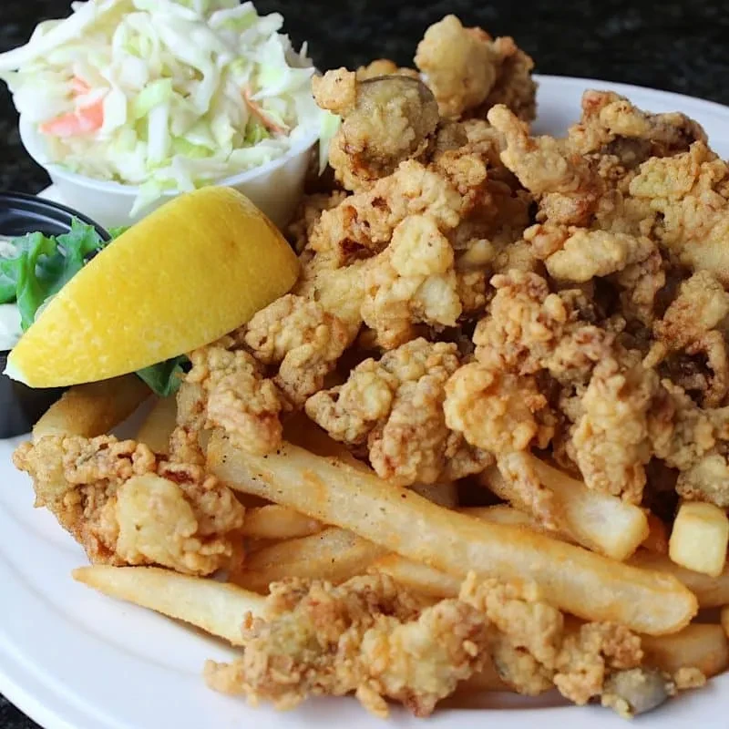 Plate of golden fried seafood, fries, coleslaw, and lemon wedge.