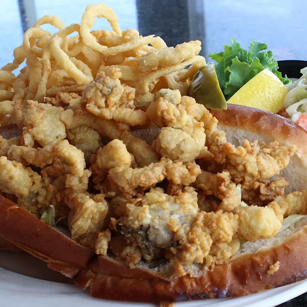 Golden-brown fried seafood roll in toasted bun, fries, lemon, pickle.
