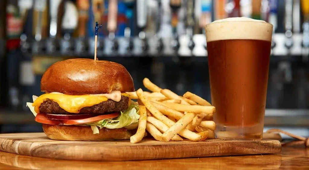 A classic cheeseburger, fries, and beer on a wooden board.