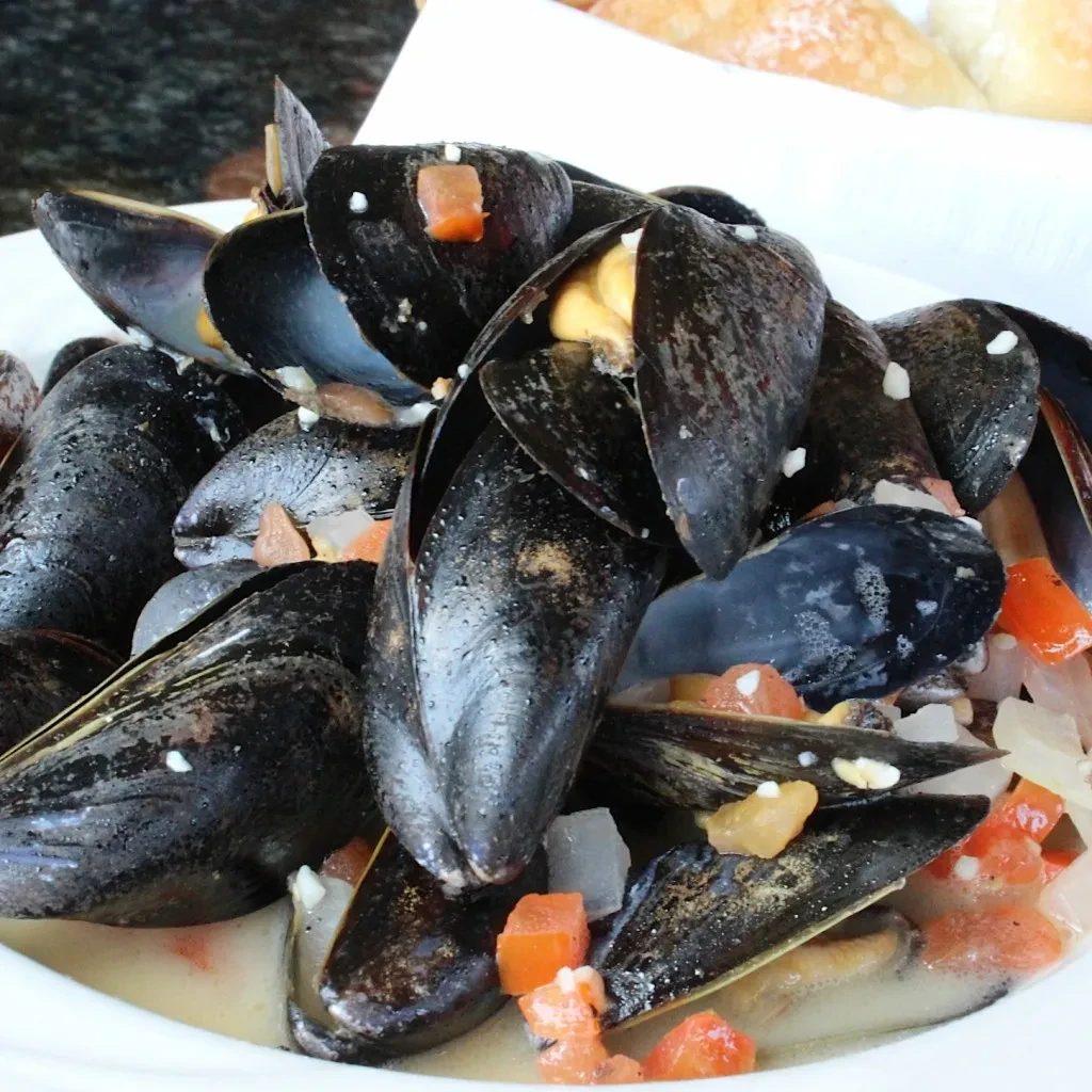 Cooked mussels in shells with creamy sauce and diced vegetables.
