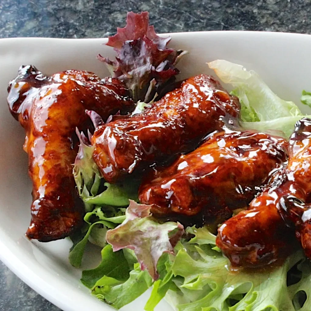 Close-up of glazed chicken wings on lettuce in a white dish.
