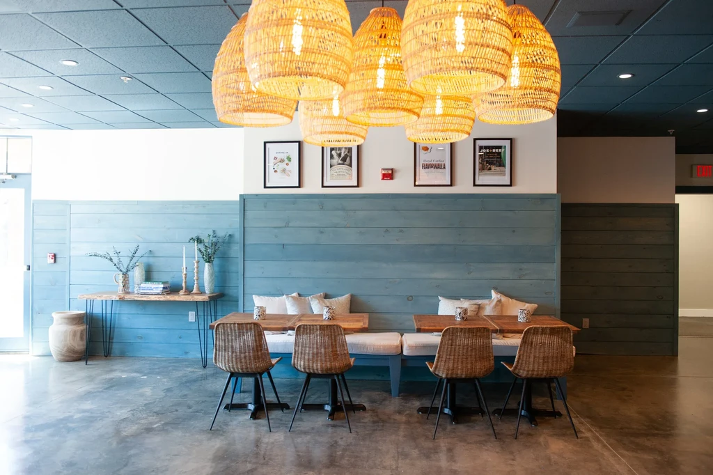 Empty modern dining area with booths, wicker chairs, and pendant lights.
