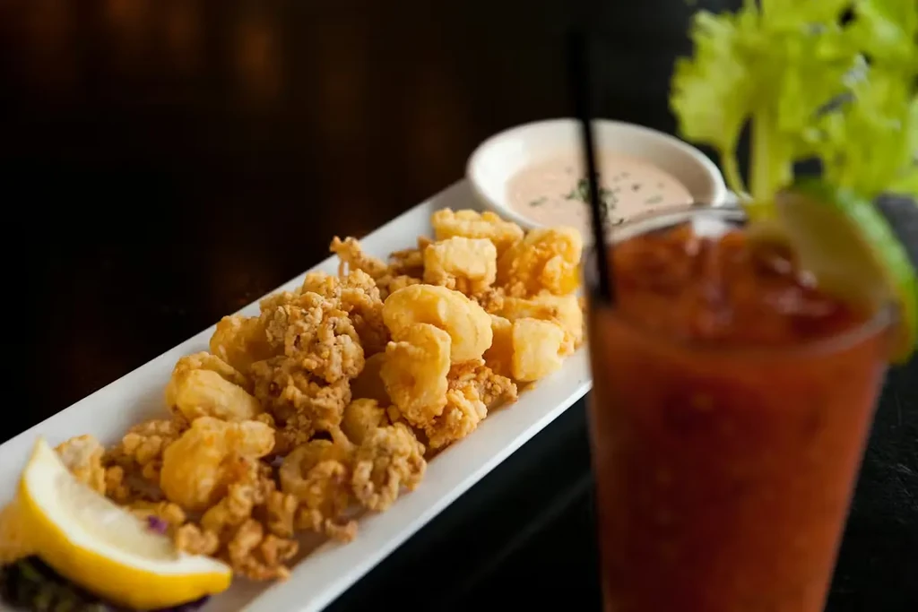 Close-up of golden-brown fried calamari, lemon, sauce, and cocktail.