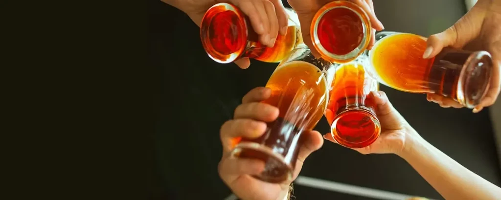 Overhead view: several hands toasting with various amber beverages.
