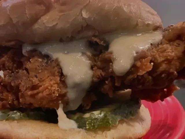 Close-up of a crispy fried chicken sandwich with dripping sauce and pickles.