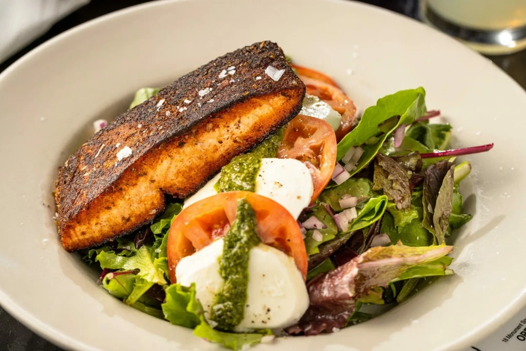 Seared salmon fillet with mixed green salad, mozzarella, and green sauce.