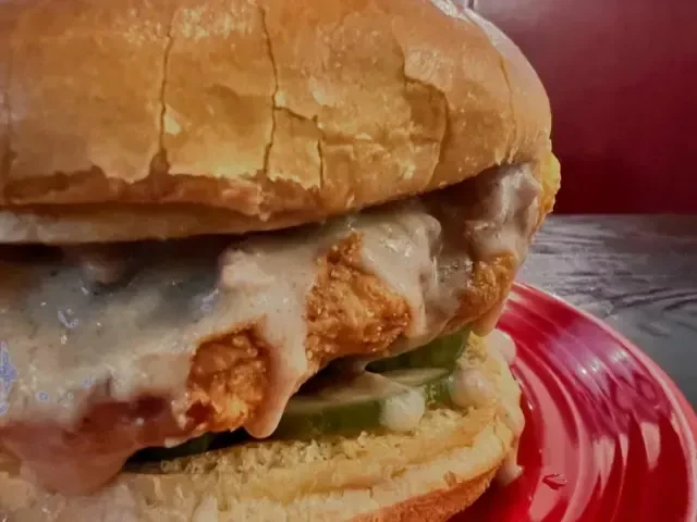 Crispy fried chicken sandwich with creamy sauce and pickles on a red plate.