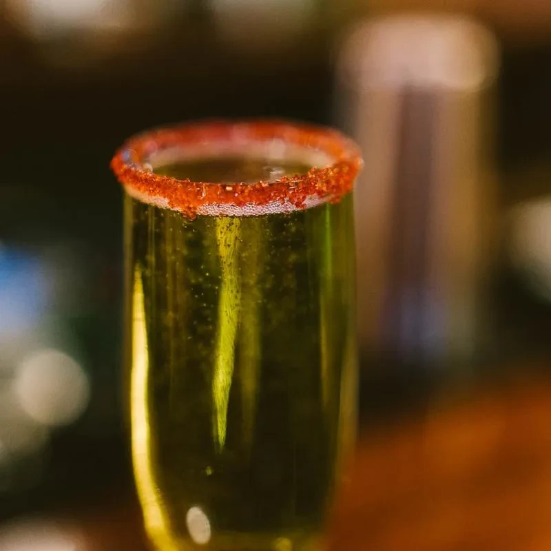Sparkling yellow drink in a champagne flute with a spiced red rim.