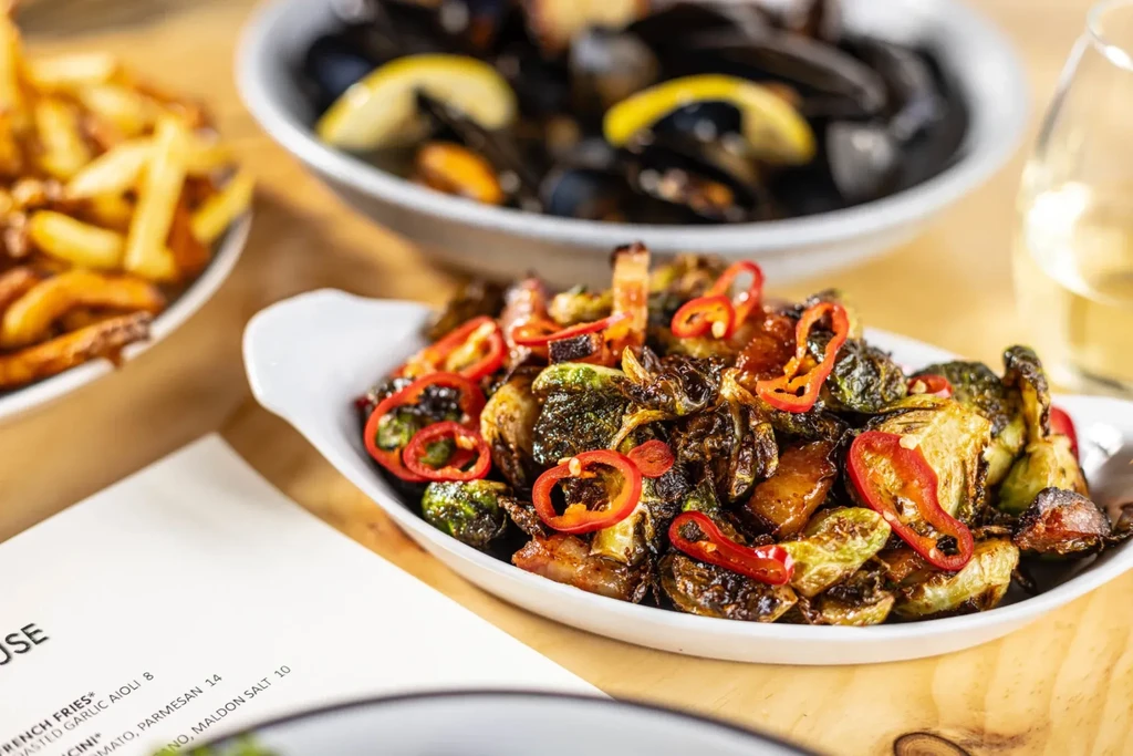 Close-up of roasted Brussels sprouts dish with mussels, fries, and wine.