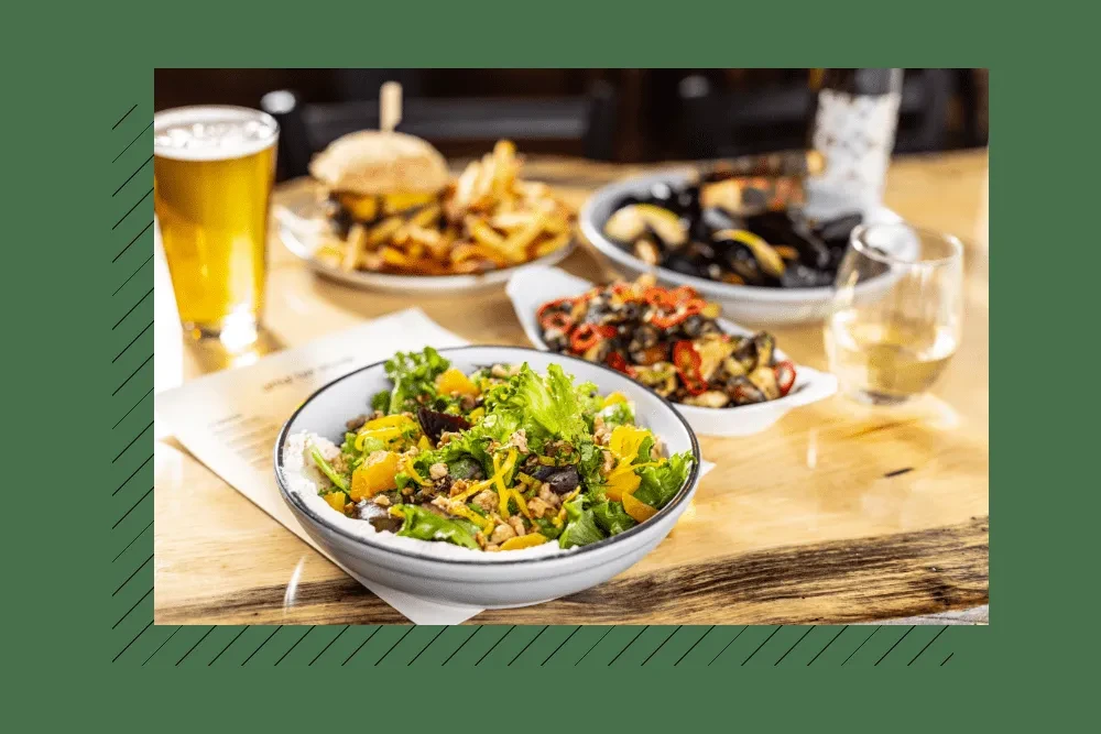 Salad, burger, fries, beer, and wine on a rustic wooden table.