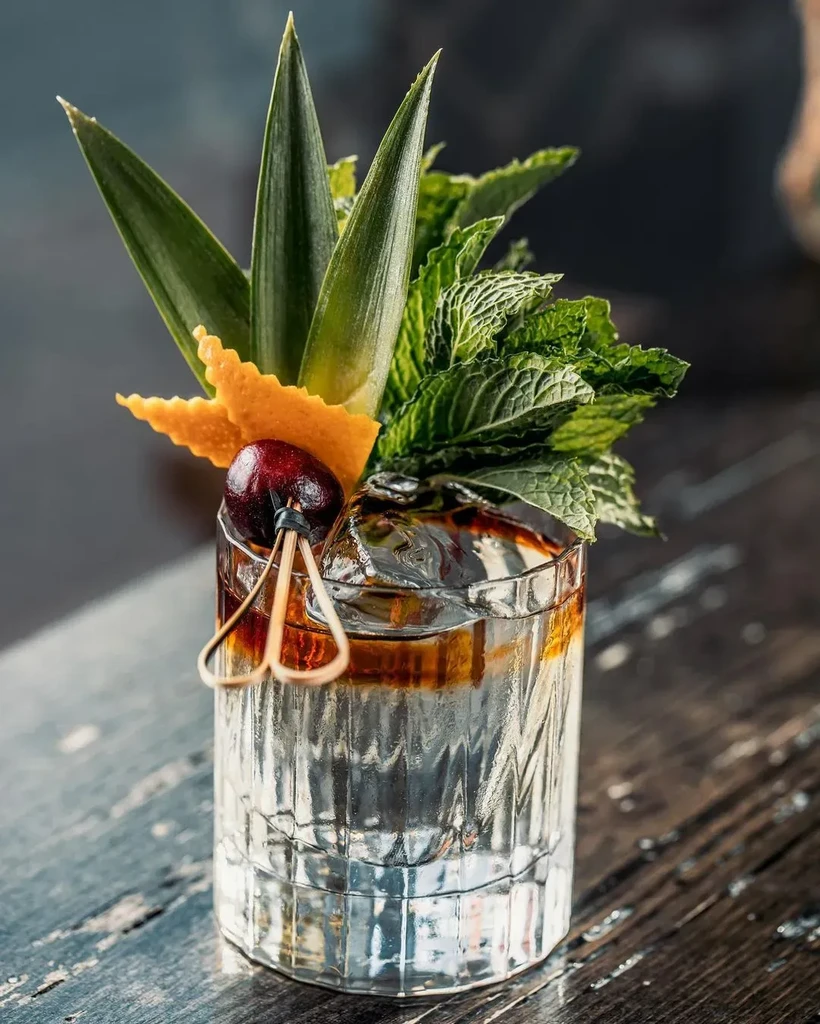 Two-toned cocktail in textured glass, garnished with mint, pineapple, cherries.