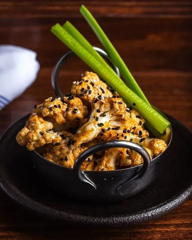 Roasted cauliflower with sesame, spices, and celery in a dark bowl.