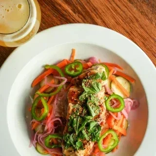 Grilled protein, colorful shredded vegetables, herbs, and sesame in a bowl.