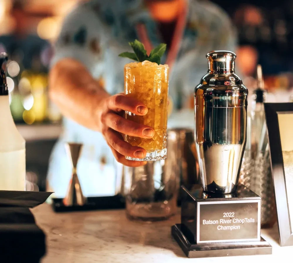 Bartender's hand holds cocktail next to 'ChopTails Champion' trophy.