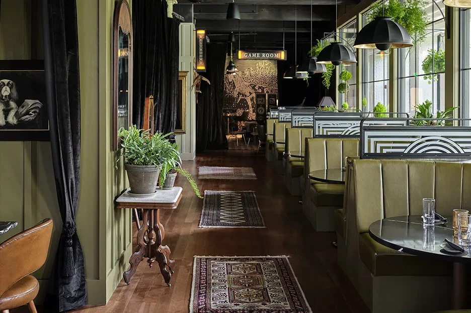 Stylish restaurant interior with olive green booths, dog portrait, and vintage decor.