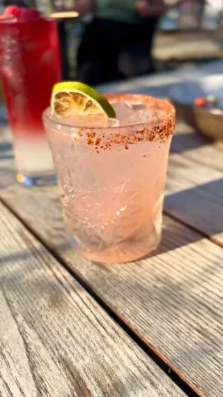 Pink drink with lime and chili-salt rim on outdoor wooden table.