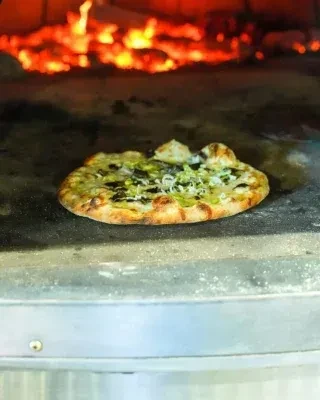 Pizza baking in a wood-fired oven with visible flames.
