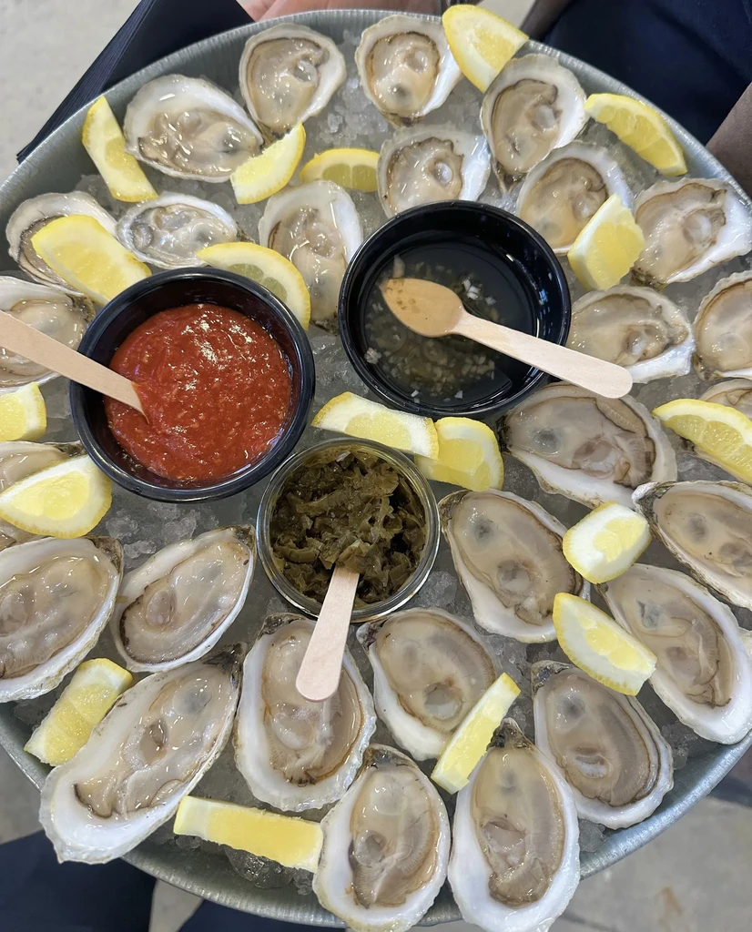 Fresh shucked oysters on ice with lemon and sauces, held by hands.