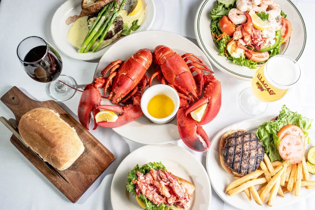 Overhead spread of lobsters, steak, salad, burgers, and drinks.