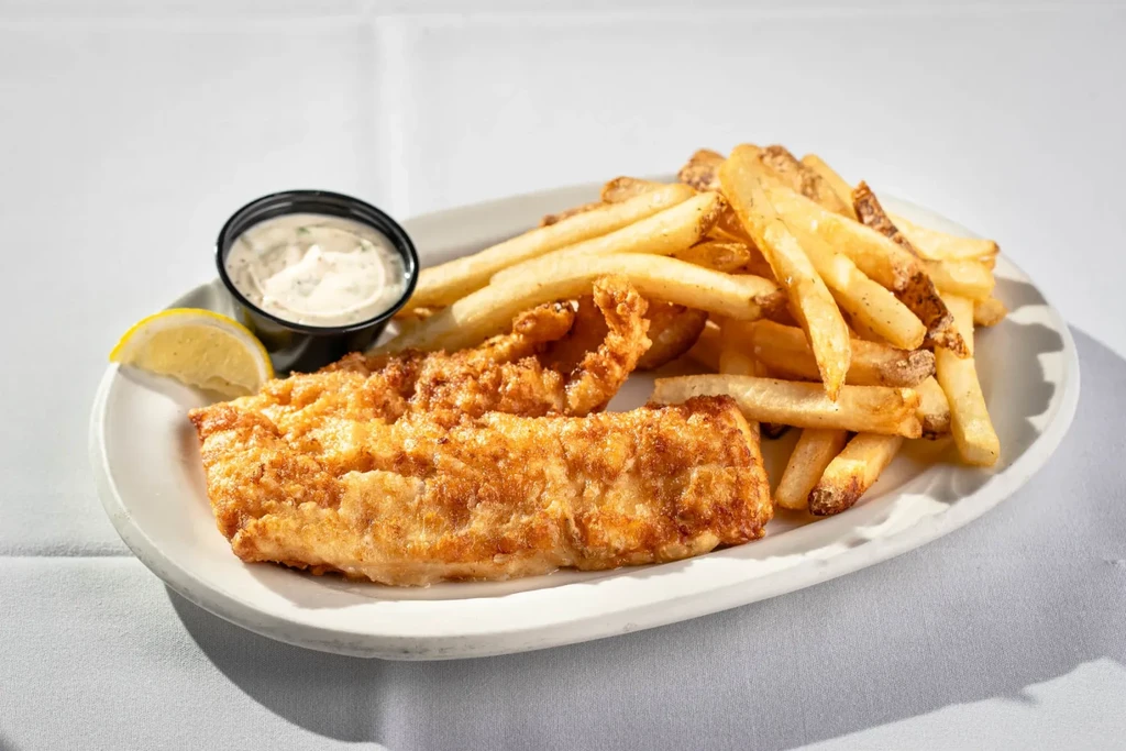 Golden-brown fish and chips, tartar sauce, and lemon on a white plate.