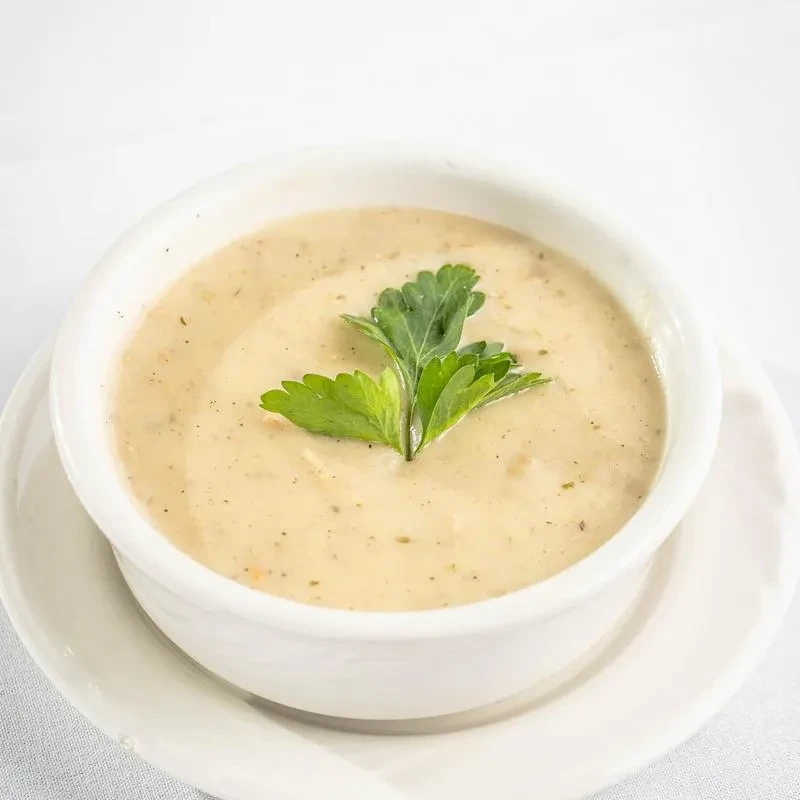 White bowl of creamy beige soup with dark specks and parsley.