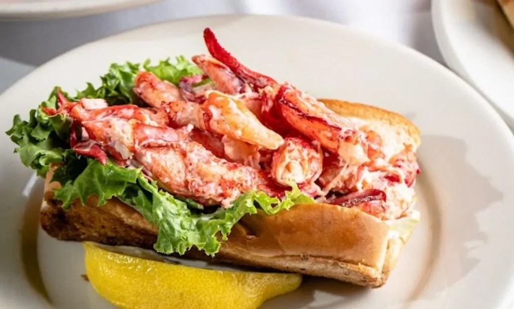 Toasted lobster roll on a plate with lettuce and lemon.