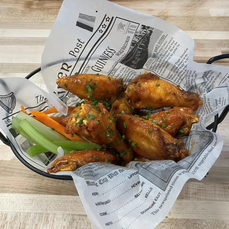 Close-up of glazed chicken wings, celery, carrots on a newspaper liner.