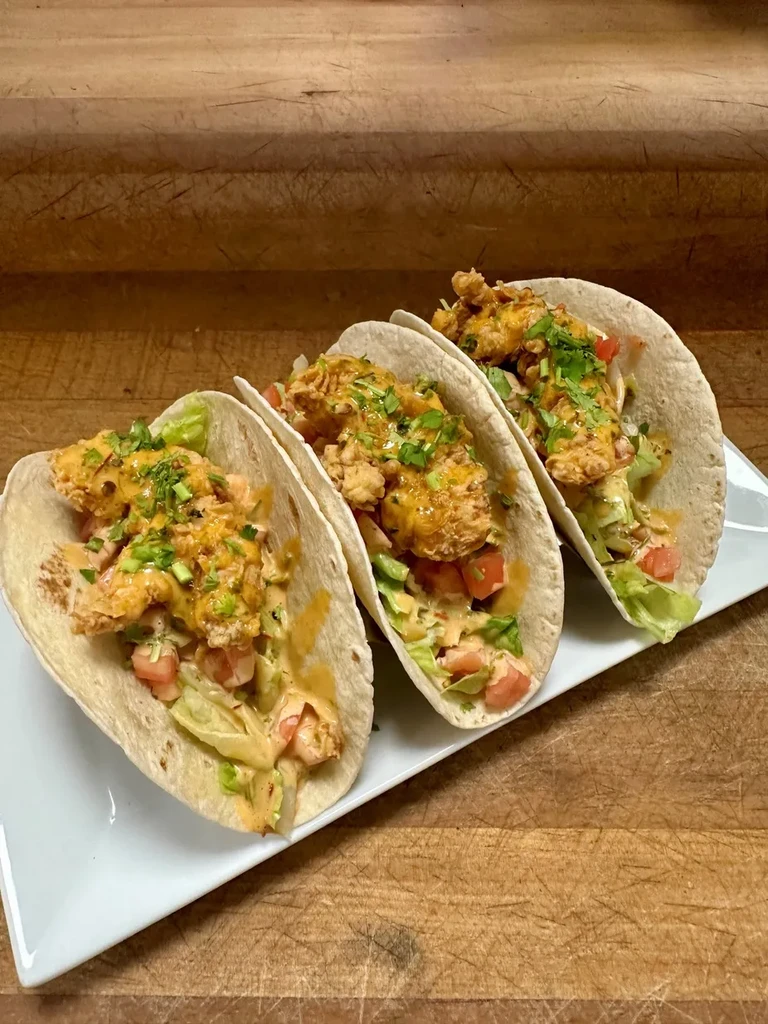 Three tacos with fried chicken or fish, vegetables, sauce on wood.