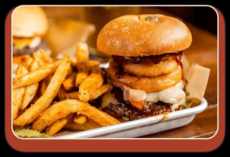 Close-up of a gourmet burger with onion rings and seasoned french fries.
