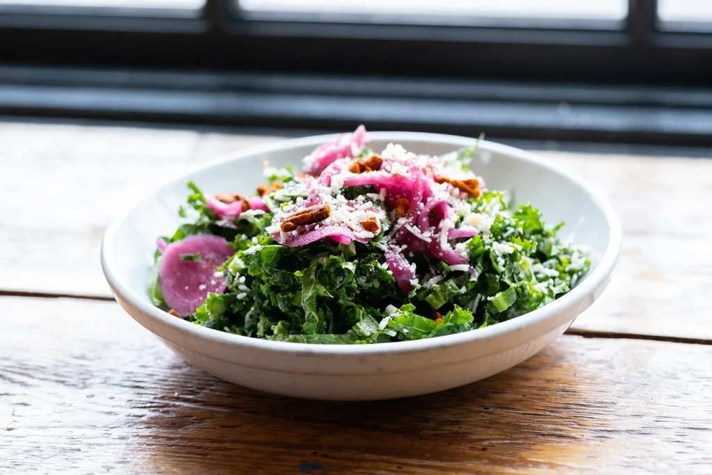 Kale salad with pickled red onions, cheese, and pecans on wood.