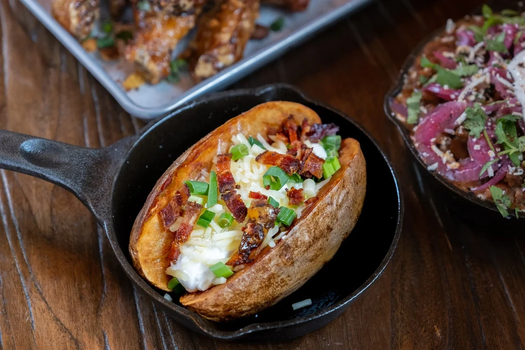 Baked potato in skillet with cheese, sour cream, bacon, green onions.