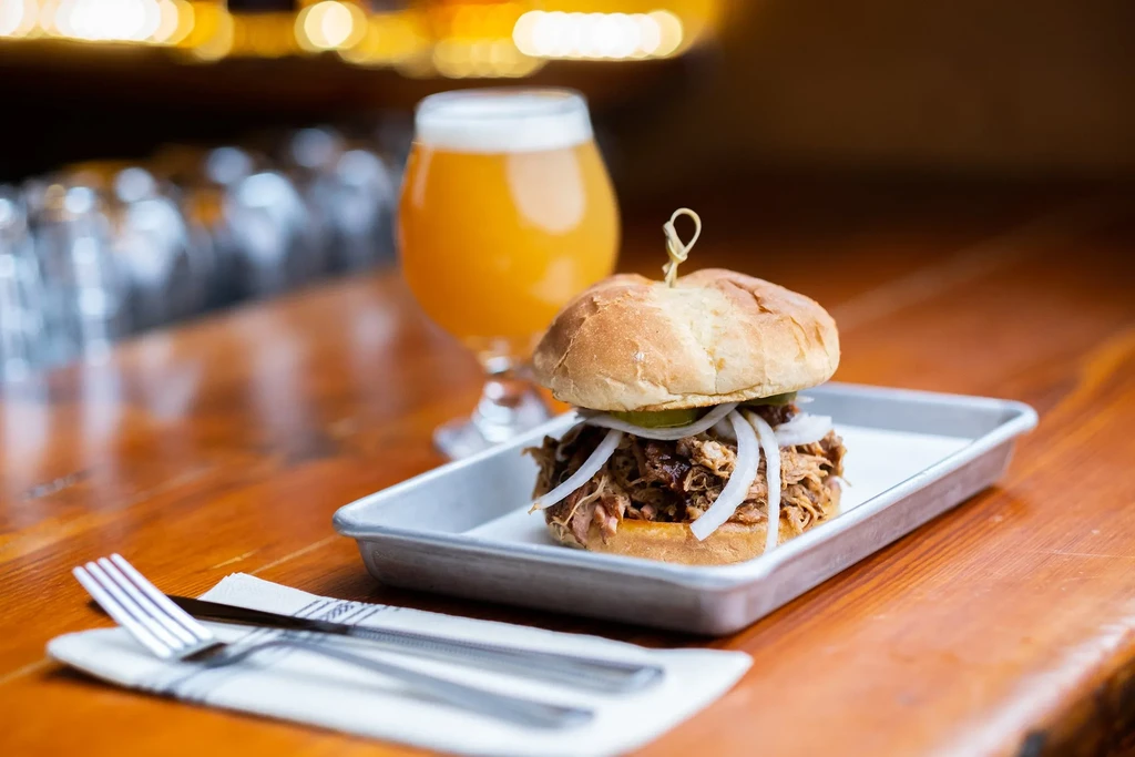Close-up of pulled pork sandwich with onions, pickles, and beer.