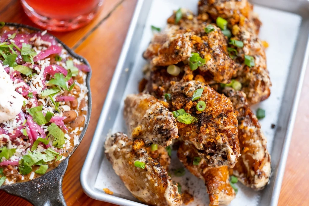 Sauced chicken wings, cheesy chili, and a drink on a wooden table.