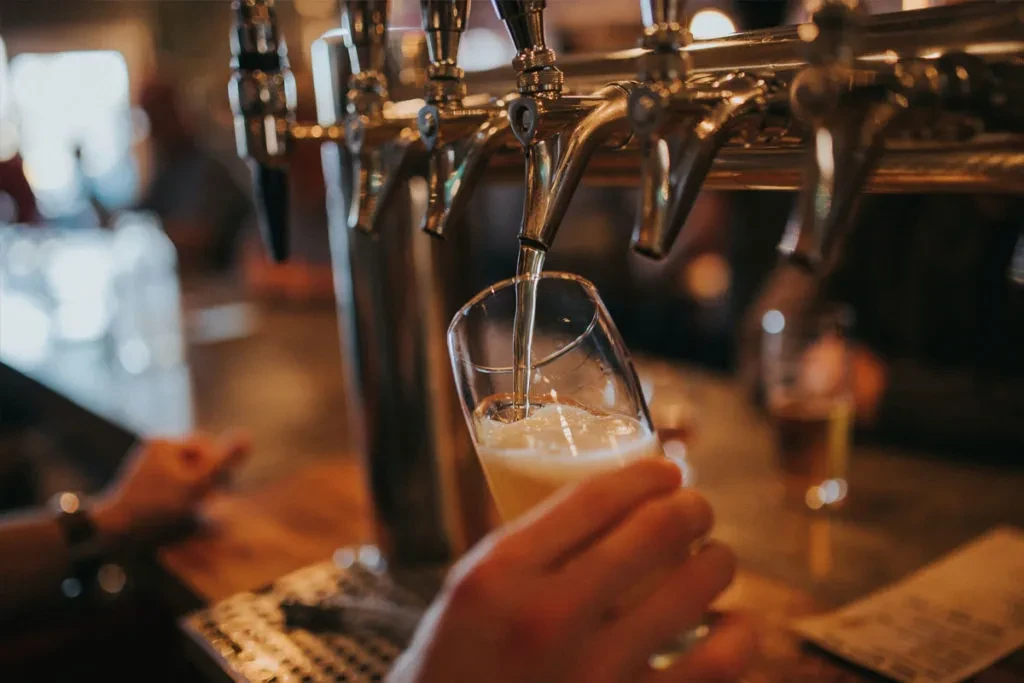 Hand holds glass as light beer pours from tap.