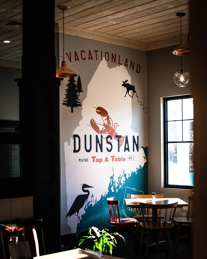 Restaurant interior features a large wall mural of a stylized Maine map.